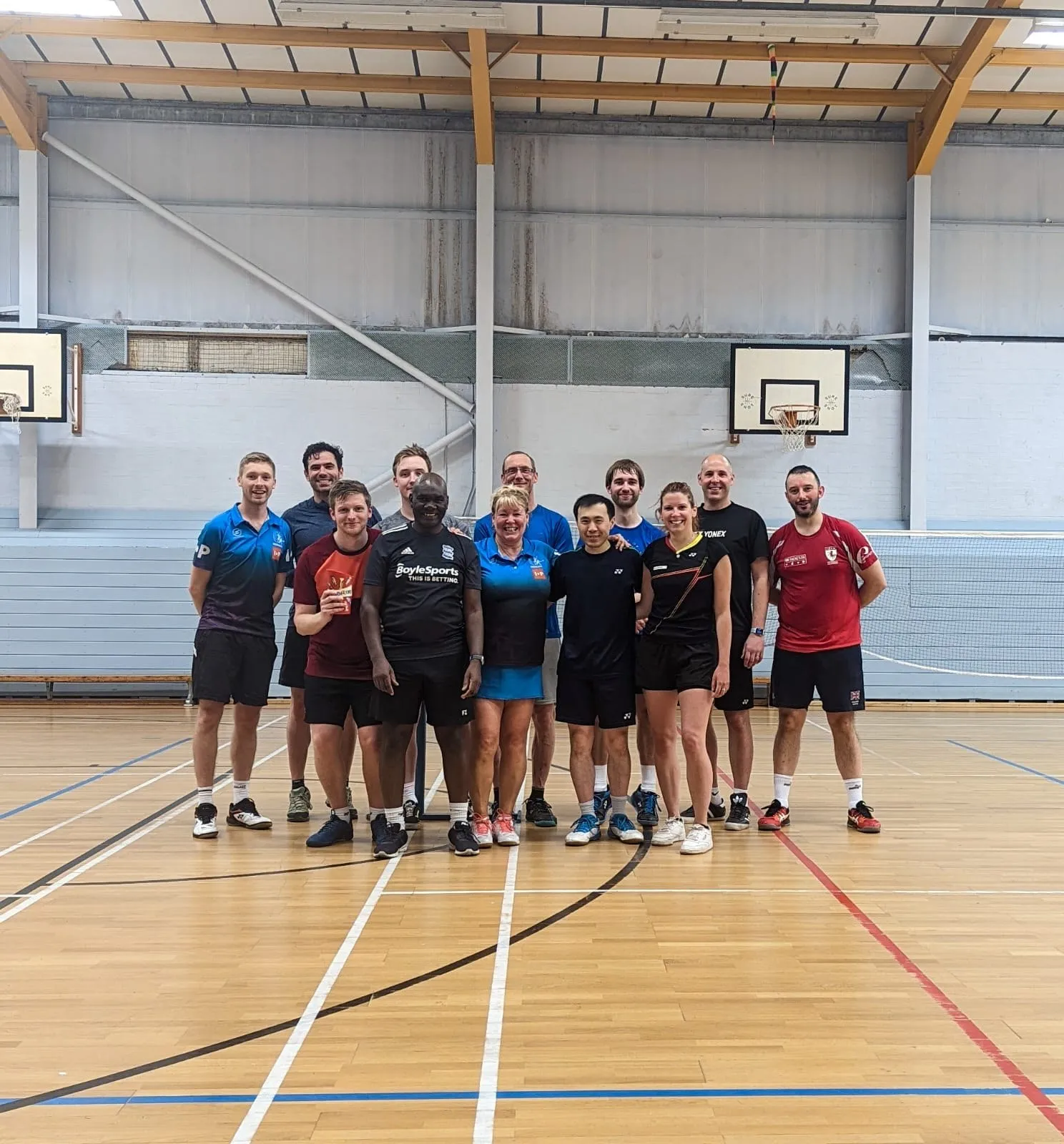Thirteen players standing together on a sports hall badminton court after a session.